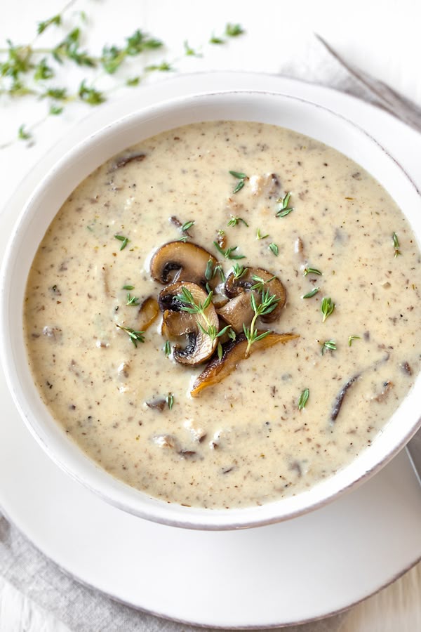 A creamy button mushroom soup topped with sliced mushrooms and thyme