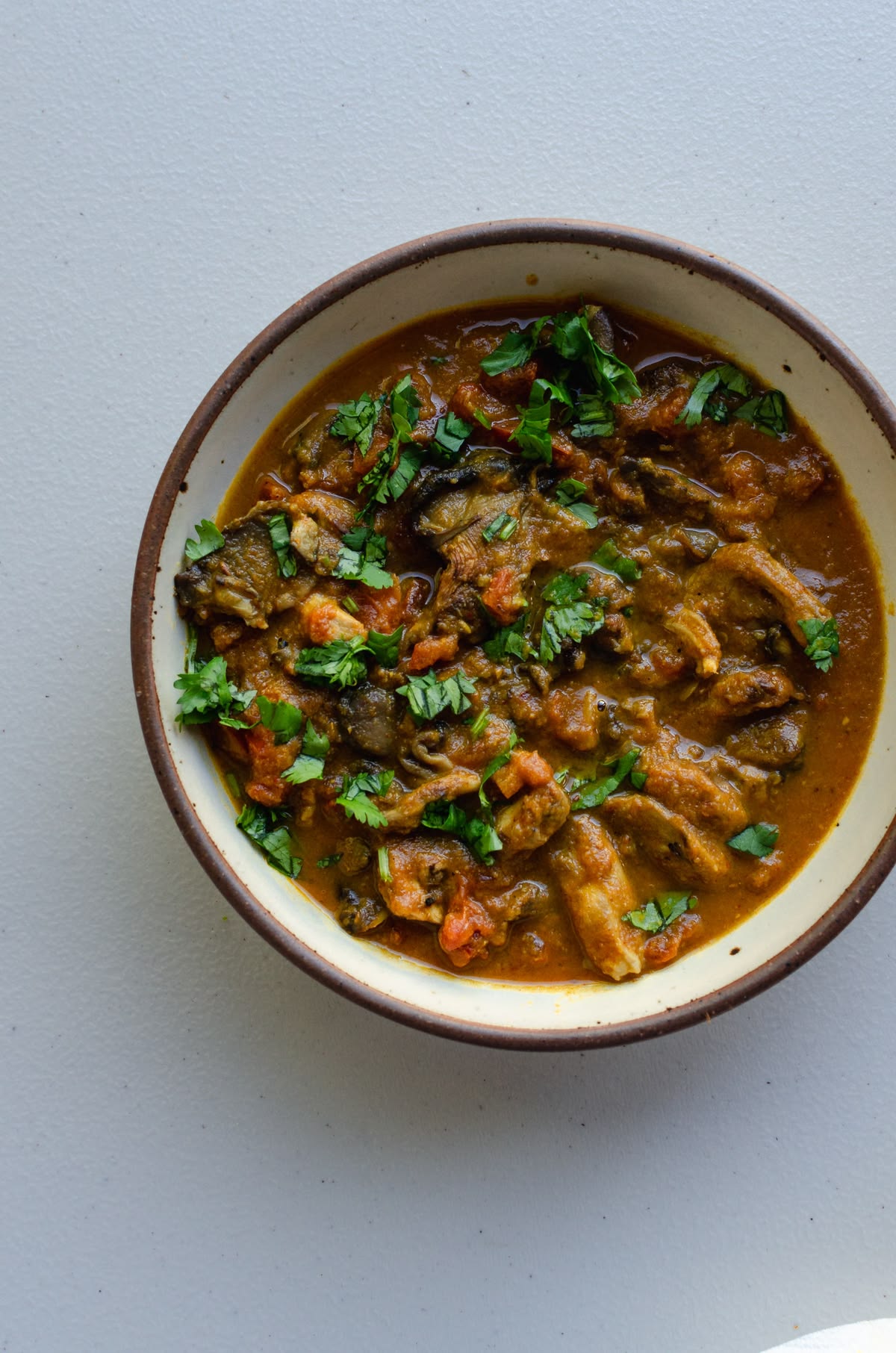 A bowl of oyster mushroom curry in a dark rim bowl, scattered with fresh coriander