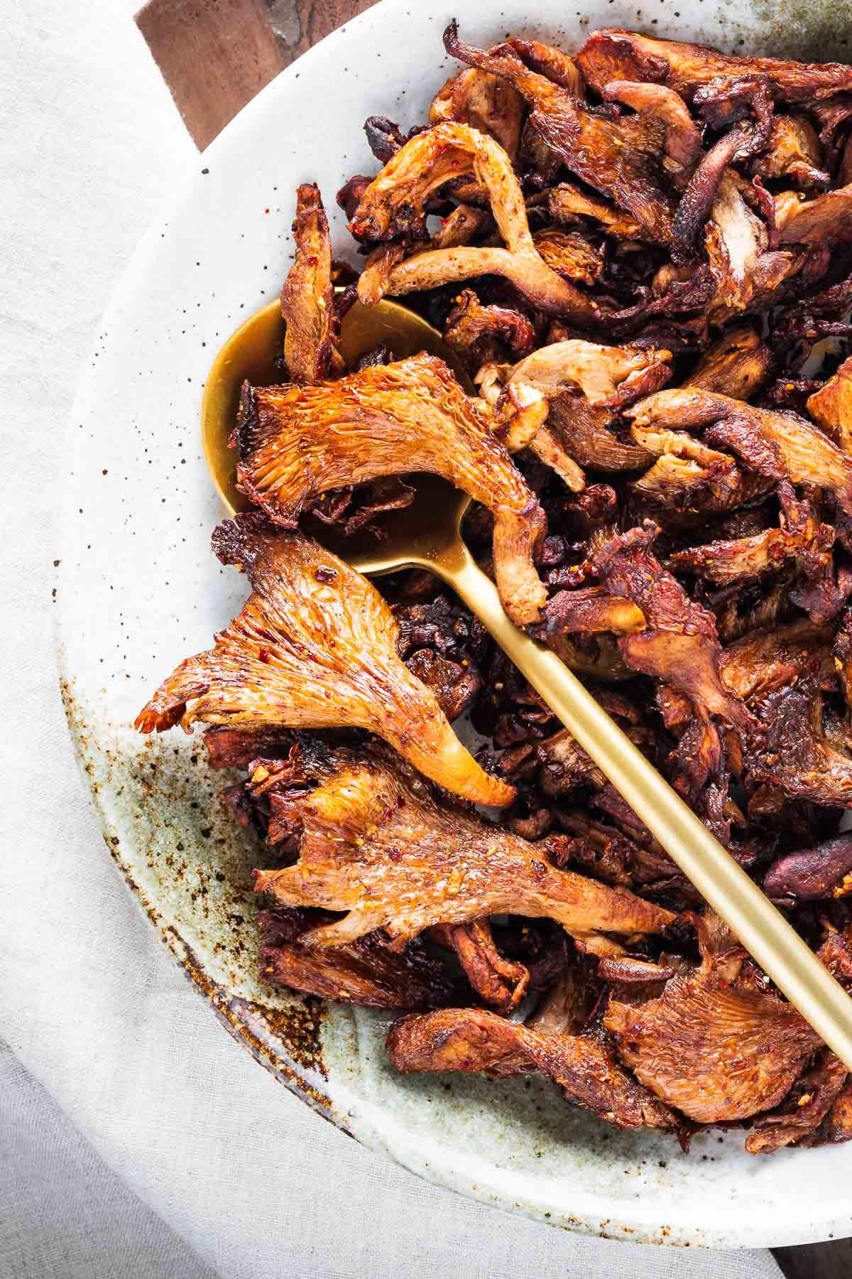 Torn pink oyster mushrooms fried until the edges are crisp and golden, served on a pale plate