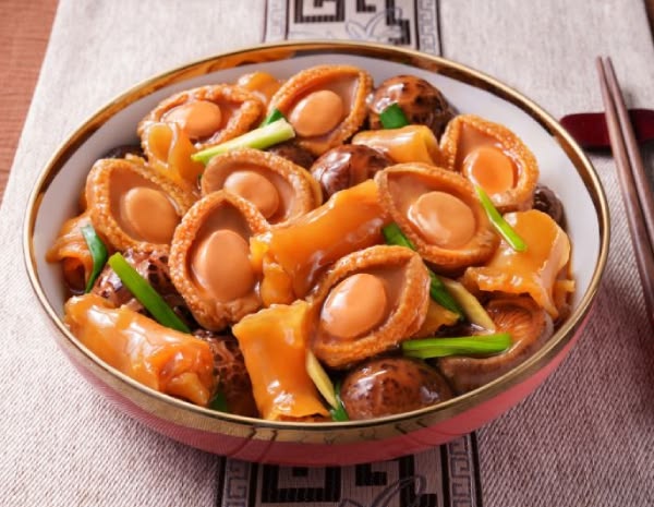 Sliced abalone-style pieces glazed in a light sauce with spring onion, served in a gold-rimmed bowl