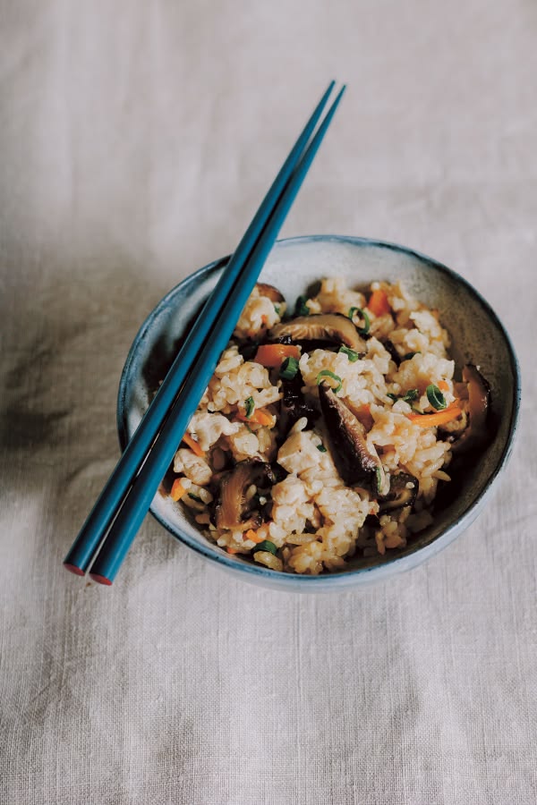 A bowl of rice studded with sliced shiitake, chopsticks resting across the rim